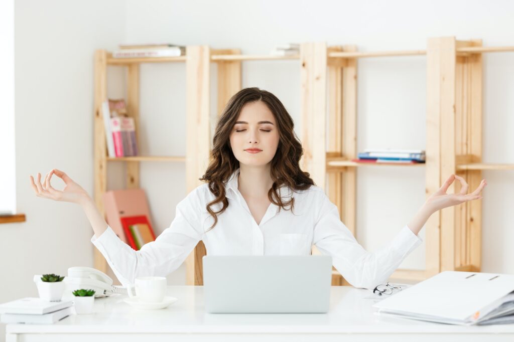 Business and Health Concept: Portrait young woman near the laptop, practicing meditation at the