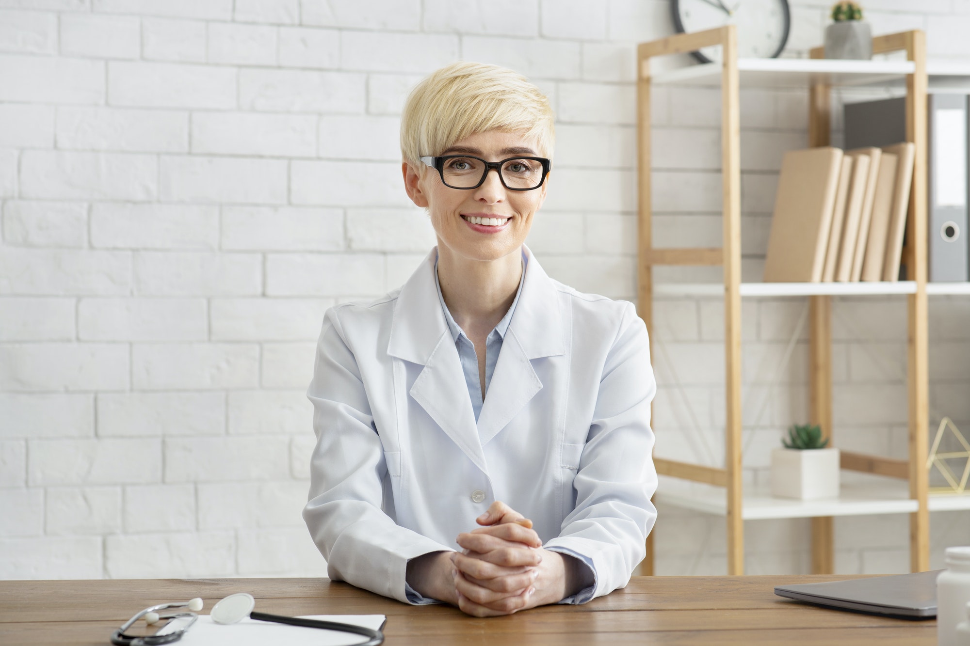 Visit to professional and health care. Smiling middle aged lady doctor sits at wooden table